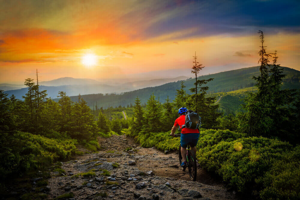 Man mountain biking on mountain trail at sunset